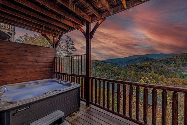 A wooden deck with a hot tub and a view of a forested valley.