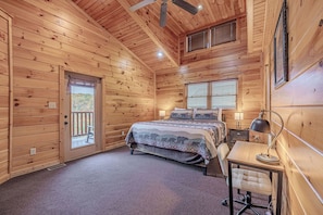 A wooden cabin bedroom with a bed, desk, chair, and ceiling fan.