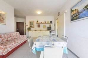 Un soggiorno con divano, un tavolo da pranzo con sedie, angolo cottura e televisione, più un quadro appeso alla parete.