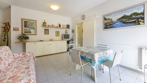 Ett kompakt bostadsutrymme med en matplats, ett litet kök och en målning som föreställer en hamn.