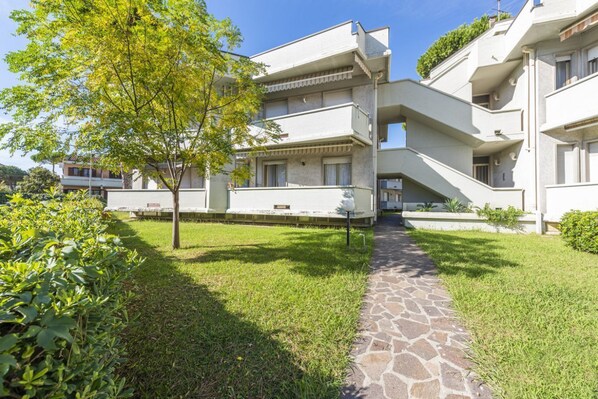 Un edificio a più piani con un vialetto in pietra che conduce all'ingresso, immerso nel verde.