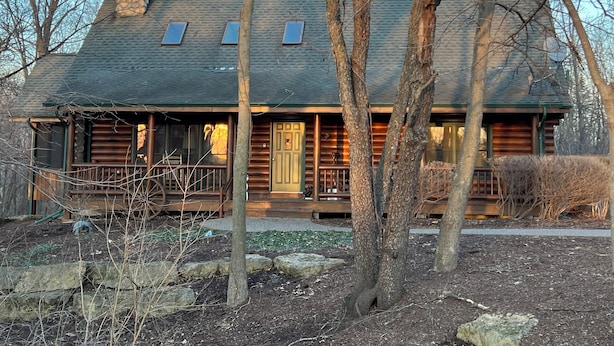 A log cabin with a stone chimney, a porch, and a view of the surrounding trees.