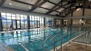 An indoor swimming pool with clear water, metal railings, and a view of the outdoors through large windows.
