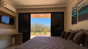 Un dormitorio con una cama grande, un escritorio y una televisión. Cuenta con un balcón con vistas a árboles y montañas.