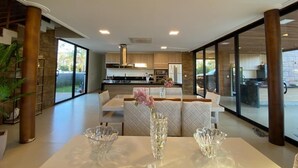 Un comedor moderno con una mesa dispuesta para dos, un florero con flores y vistas a la cocina y al área exterior.