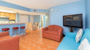 A living room with a sofa, a TV, and a kitchen area with stools. - Walk to Beach - Heart of Entertainment District 1 Bedroom Home by RedAwning (South Padre Island)