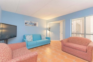 Una sala de estar con un sofá azul, un sofá rosa y un televisor de pantalla plana.