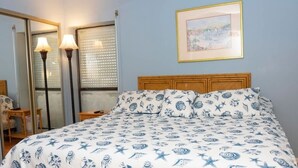 A bedroom with a bed, two bedside lamps, a framed picture on the wall, and a window with blinds. - Walk to Beach - Heart of Entertainment District 1 Bedroom Home by RedAwning (South Padre Island)