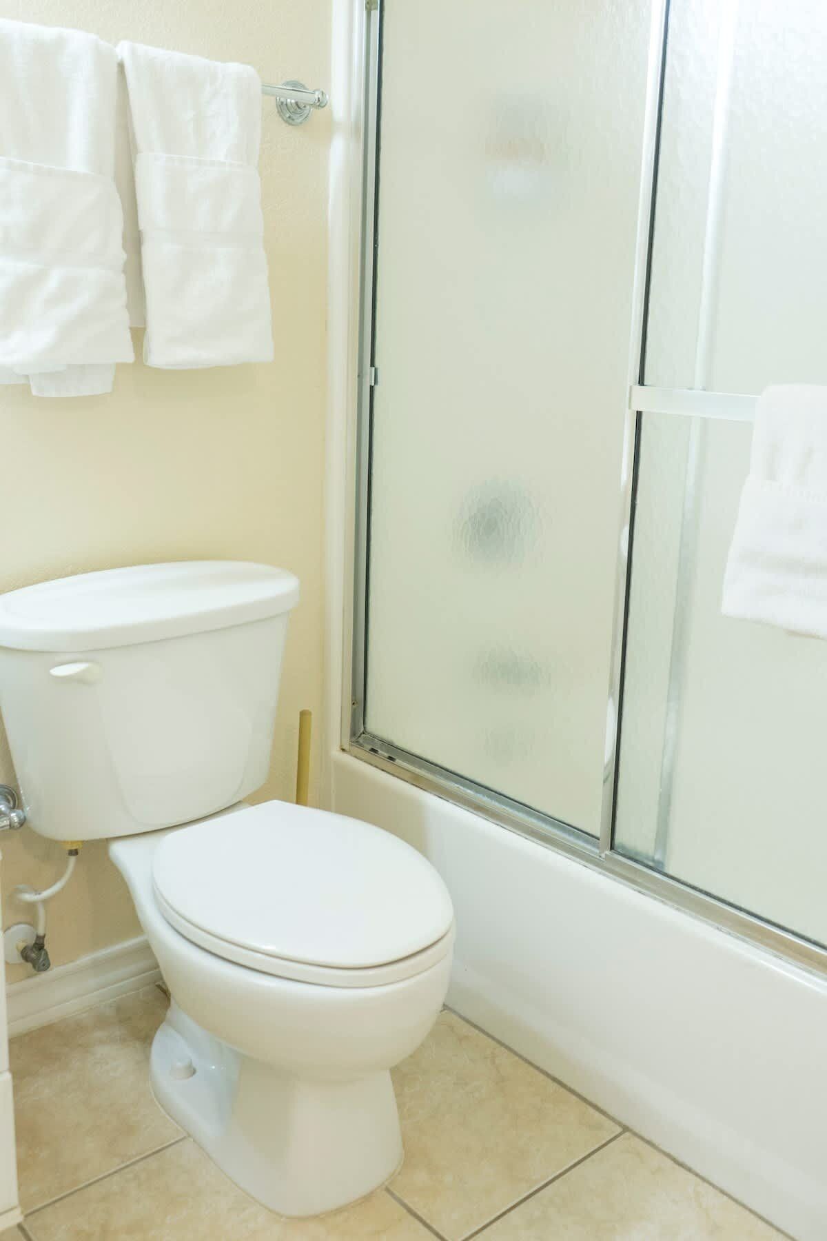 Un baño con inodoro, mampara de vidrio para la ducha y dos toallas blancas colgadas en la pared.
