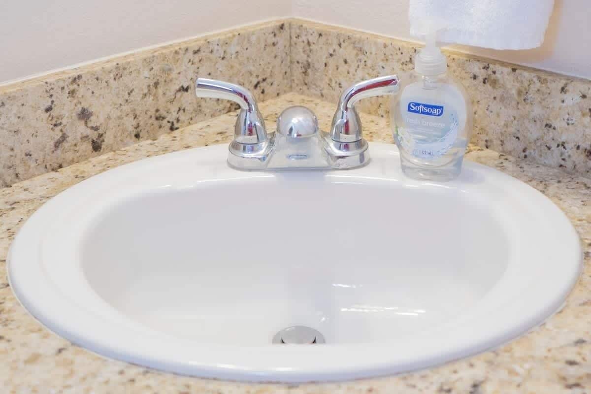 A white sink with a single faucet and a bottle of Softsoap.