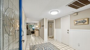 A hallway with a tiled floor, a blue door, a patterned rug, and a 'BEACH' sign on the wall.