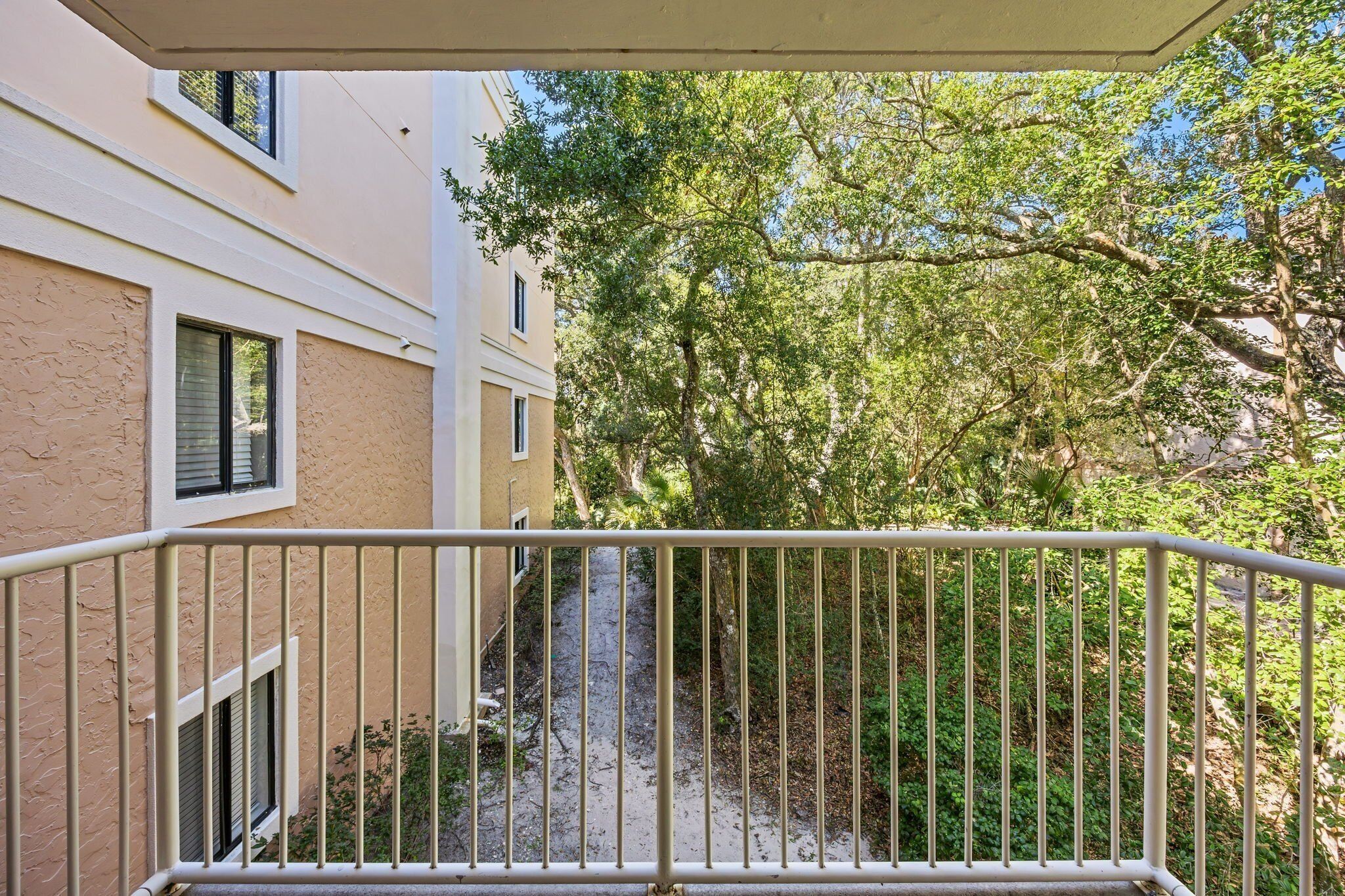 En balkon med gelænder i metal, der giver udsigt over en smal sti mellem træer og bygninger.