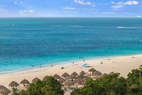 A beach with clear turquoise water, thatched-roof huts, and a sandy shore.