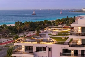 Un hotel moderno con terraza en la azotea, piscina y vistas al océano con veleros.