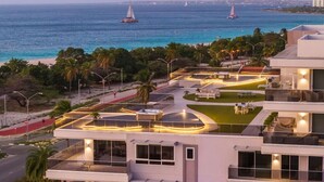 Un hotel moderno con terraza en la azotea, piscina y vistas al océano con veleros.
