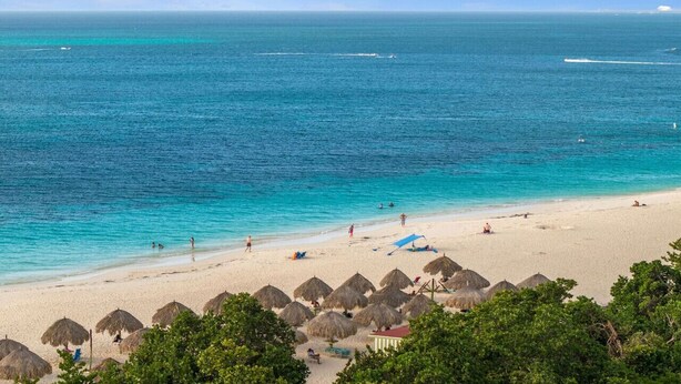 Una playa con aguas turquesas transparentes, cabañas de techo de paja y una orilla arenosa.