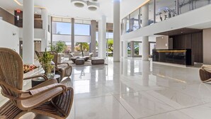 Un vestíbulo espacioso con techos altos, ventanas amplias y una zona de estar central con mobiliario de mimbre.