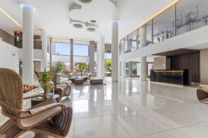 A spacious lobby with high ceilings, large windows, and a central seating area with wicker furniture.