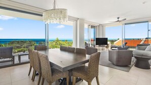 Un comedor espacioso con vista al océano, un gran candelabro y muebles modernos.
