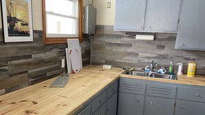 A kitchen with grey cabinets, a wooden countertop, a built-in sink, and a tiled backsplash. - Little Bluff Inn (Trempealeau)