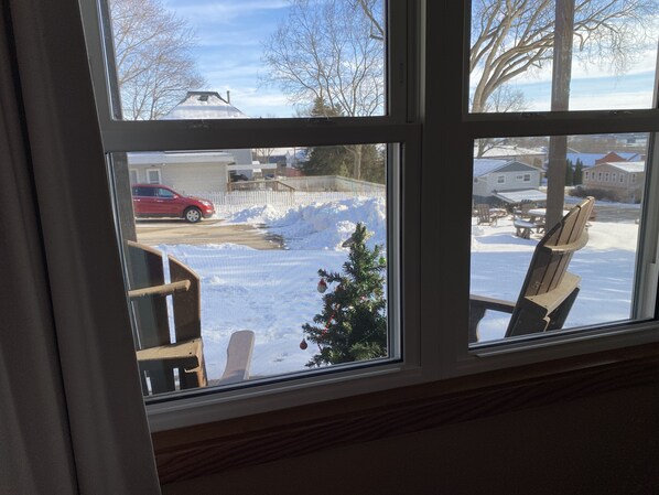 A window with a view of a snowy outdoor area, including a red car and a small Christmas tree.