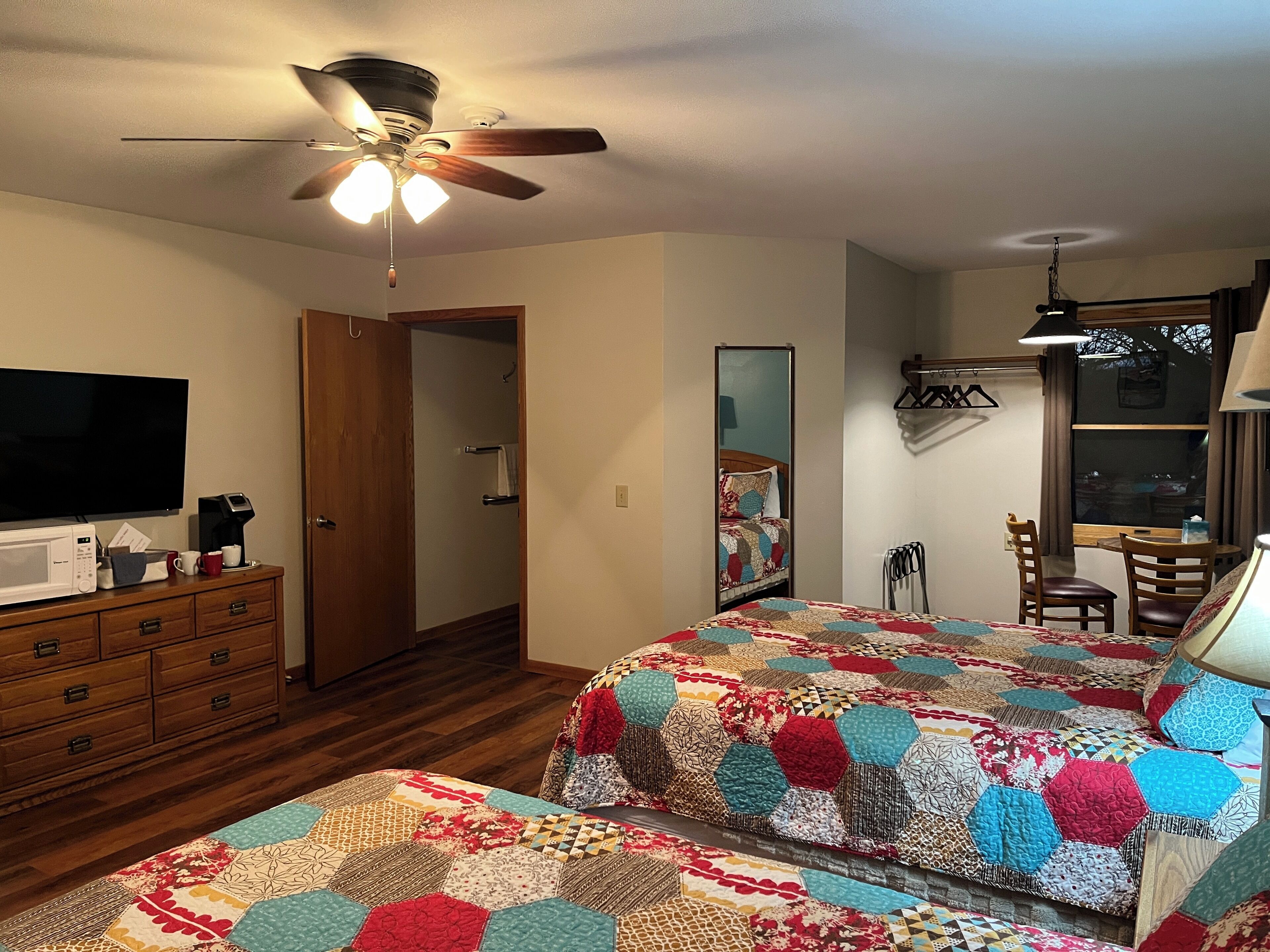 A bedroom with two beds, a ceiling fan, a TV, a microwave, and a wooden dresser.