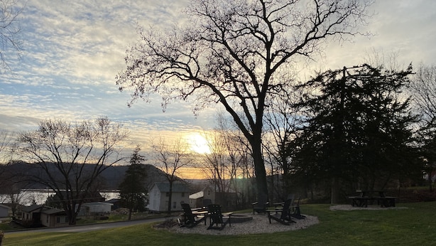 A park with picnic tables and chairs, a large tree, and a lake in the background. - Little Bluff Inn (Trempealeau)