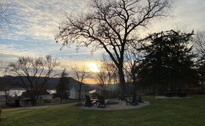 A park with picnic tables and chairs, a large tree, and a lake in the background. - Little Bluff Inn (Trempealeau)