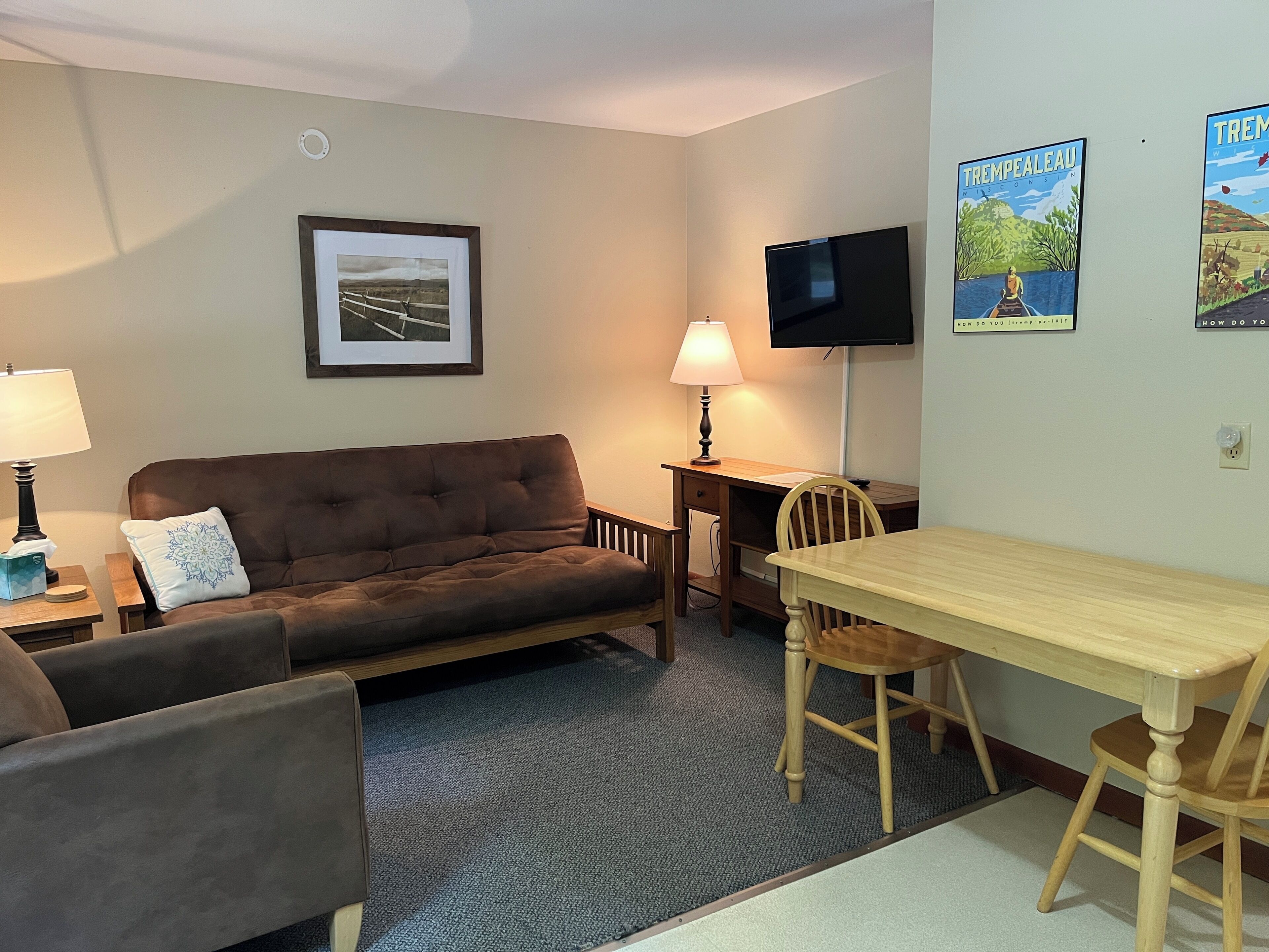 A furnished room with a brown sofa, a wooden table, a TV, and a framed picture on the wall.