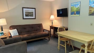 A furnished room with a brown sofa, a wooden table, a TV, and a framed picture on the wall.
