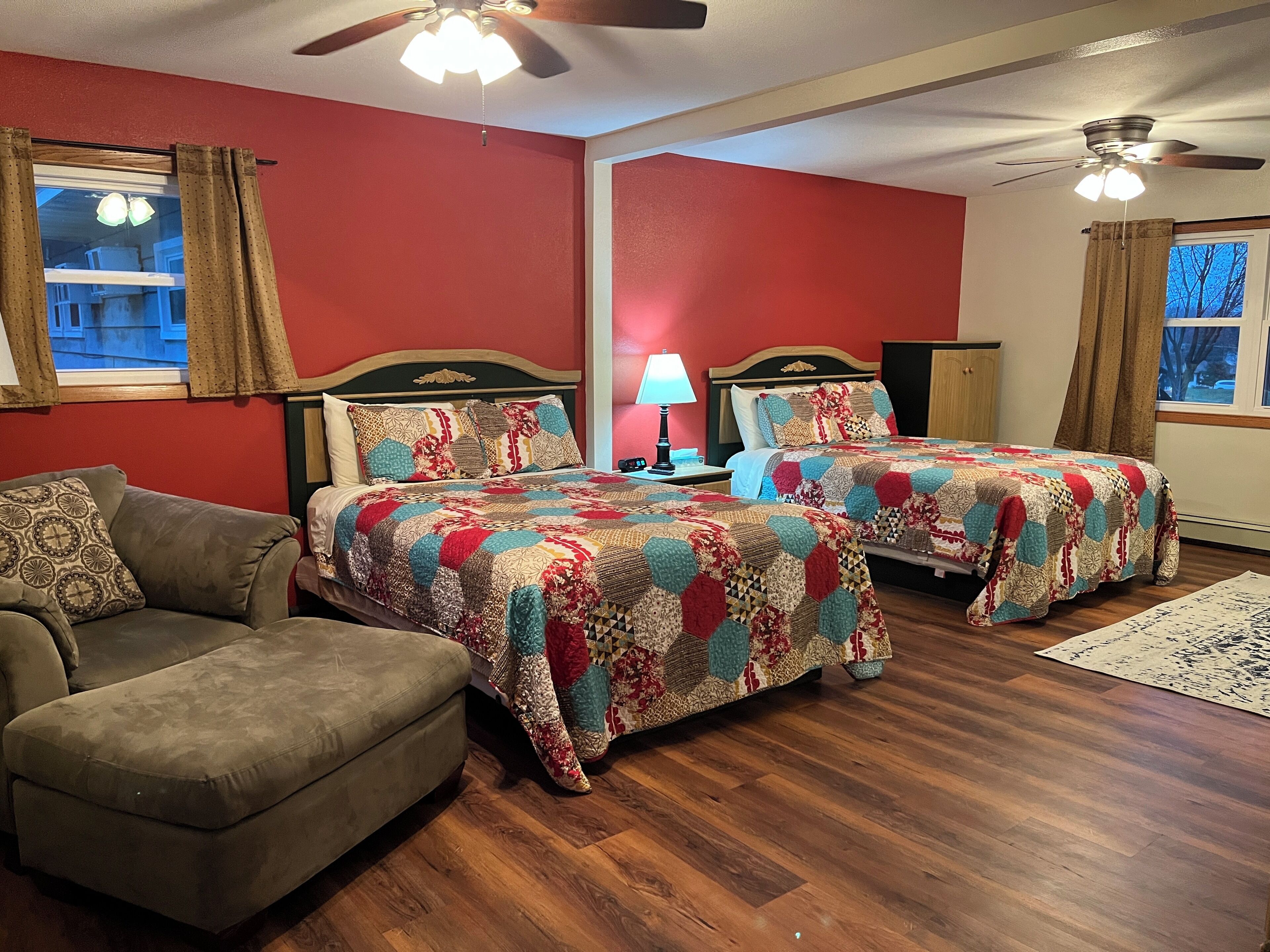 A room with two beds, a sofa, a wooden floor, and a ceiling fan.