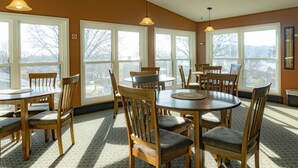 A dining area with multiple wooden tables and chairs, large windows with a view of trees, and pendant lights. - Little Bluff Inn (Trempealeau)