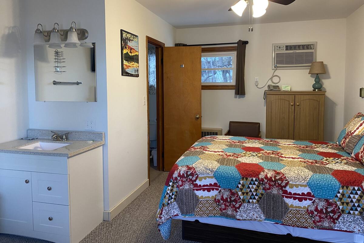Un dormitorio con cama, armario de madera, baño con lavamanos y ventilador de techo.