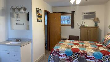 A bedroom with a bed, a wooden wardrobe, a bathroom with a sink, and a ceiling fan.