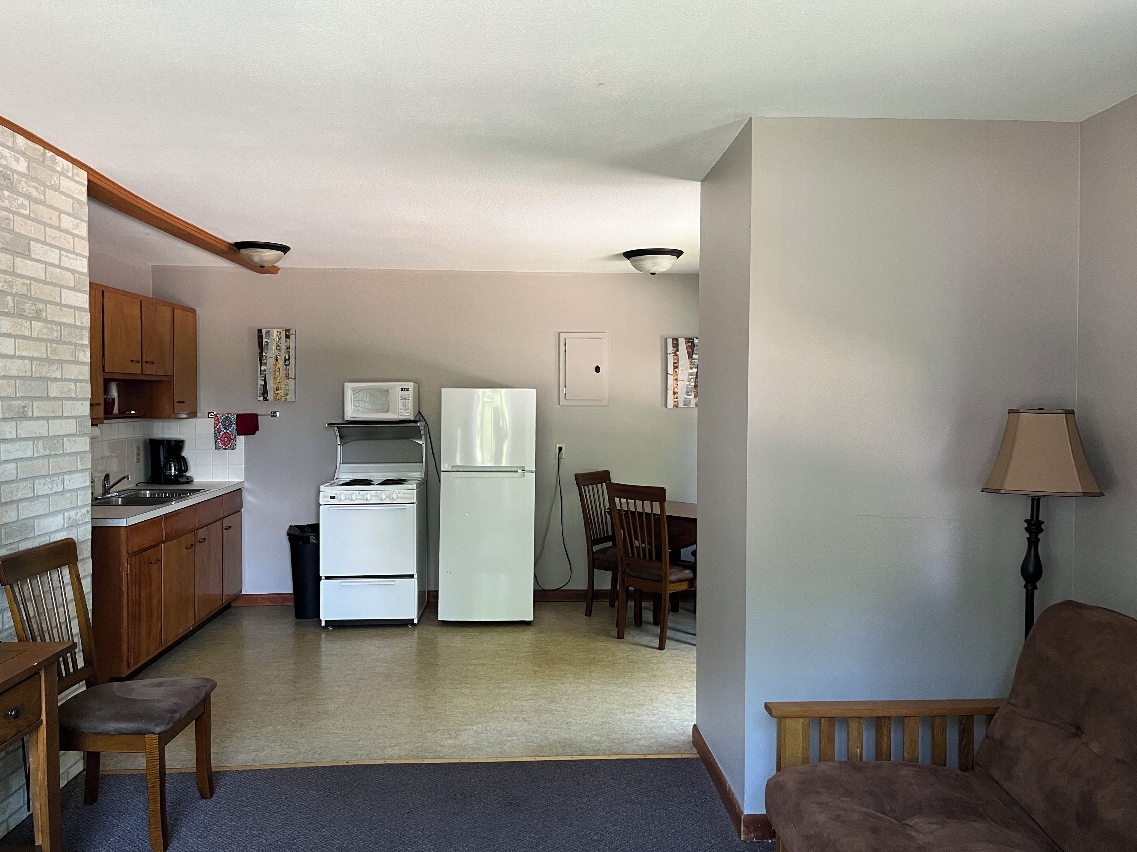 A compact kitchen with a stove, microwave, and refrigerator. There is a dining table with chairs and a lamp.