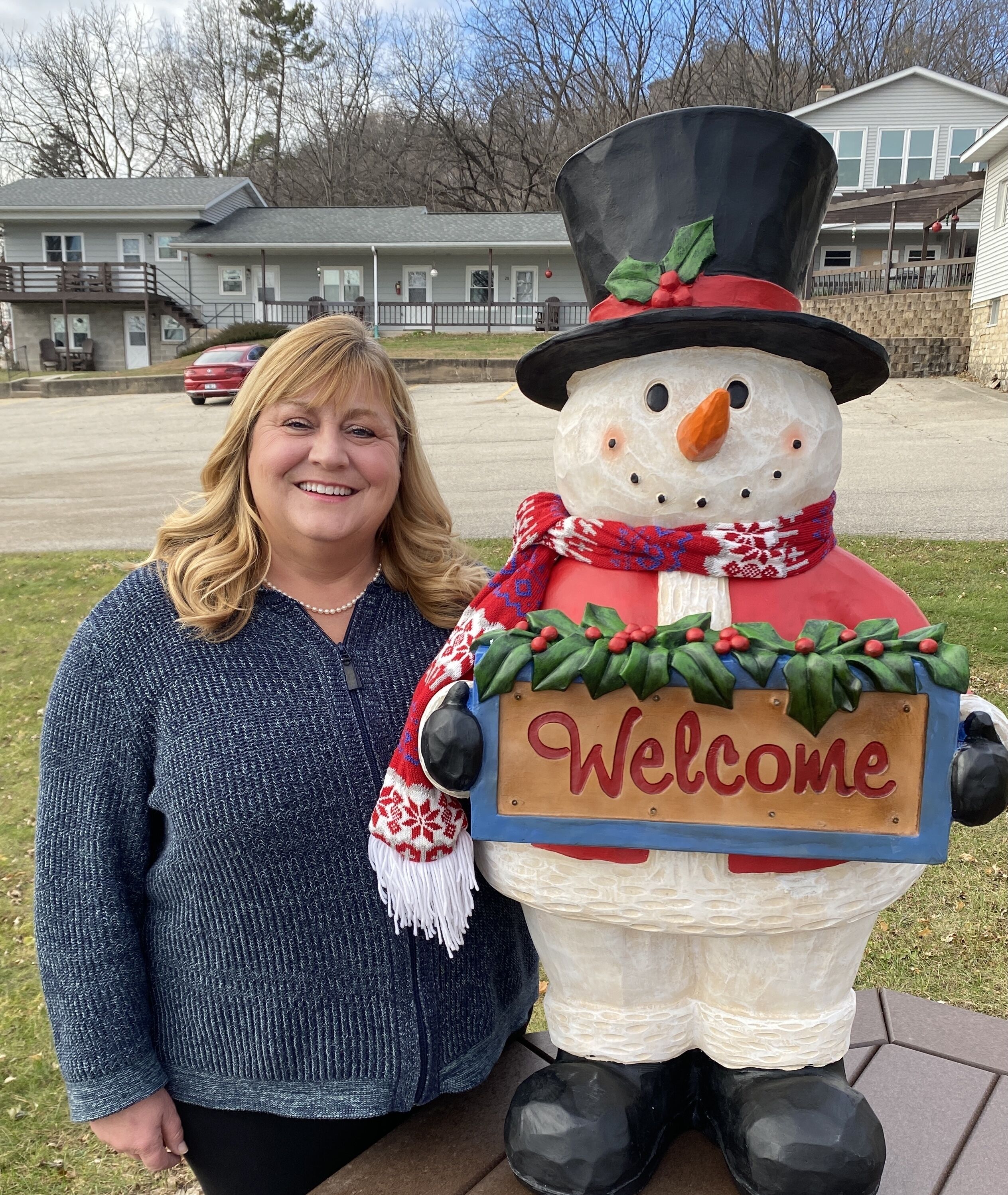 A person standing next to a large snowman decoration with a 'Welcome' sign.