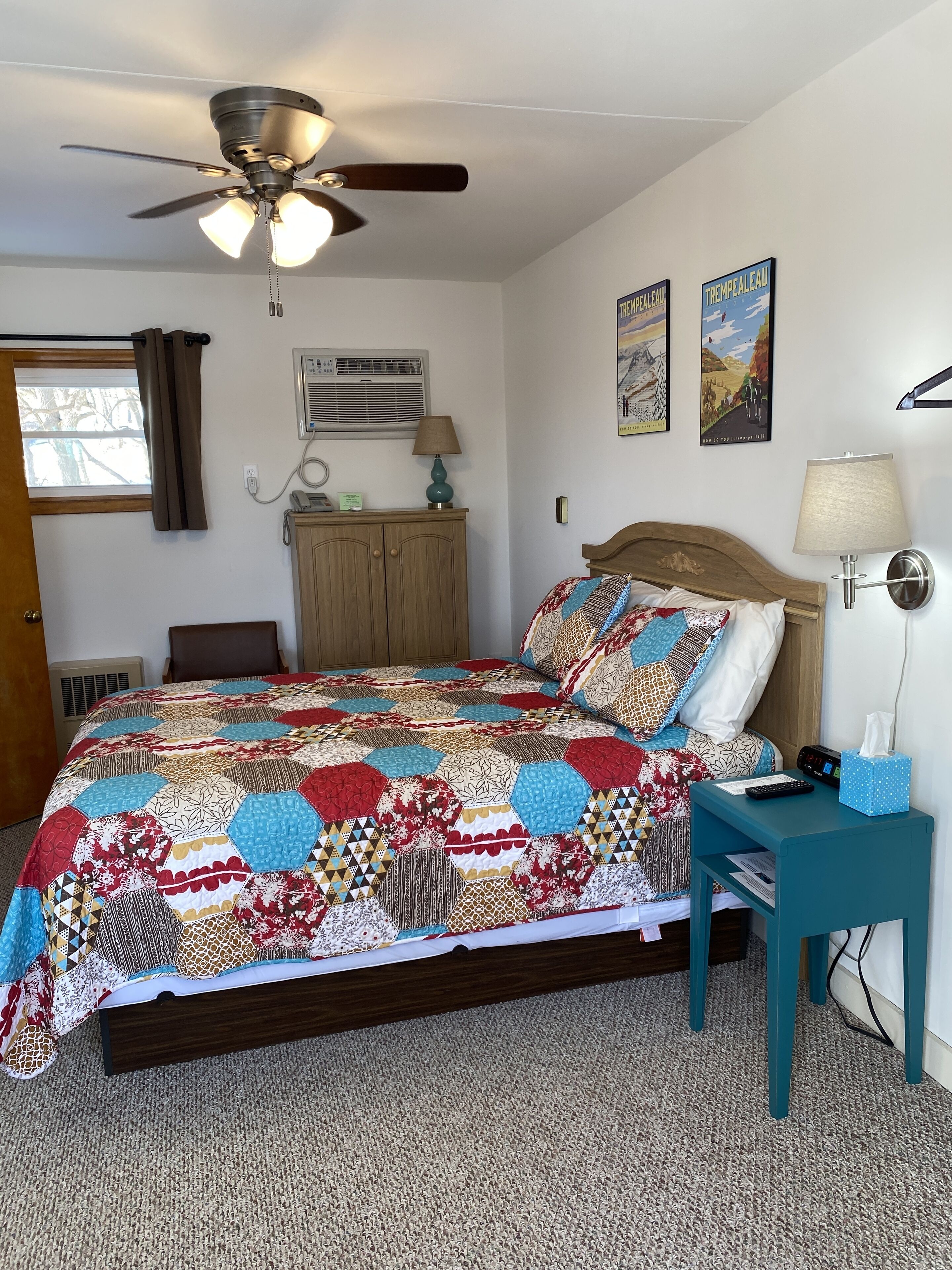 A bedroom with a bed, a nightstand, a ceiling fan, a window with curtains, and wall art.