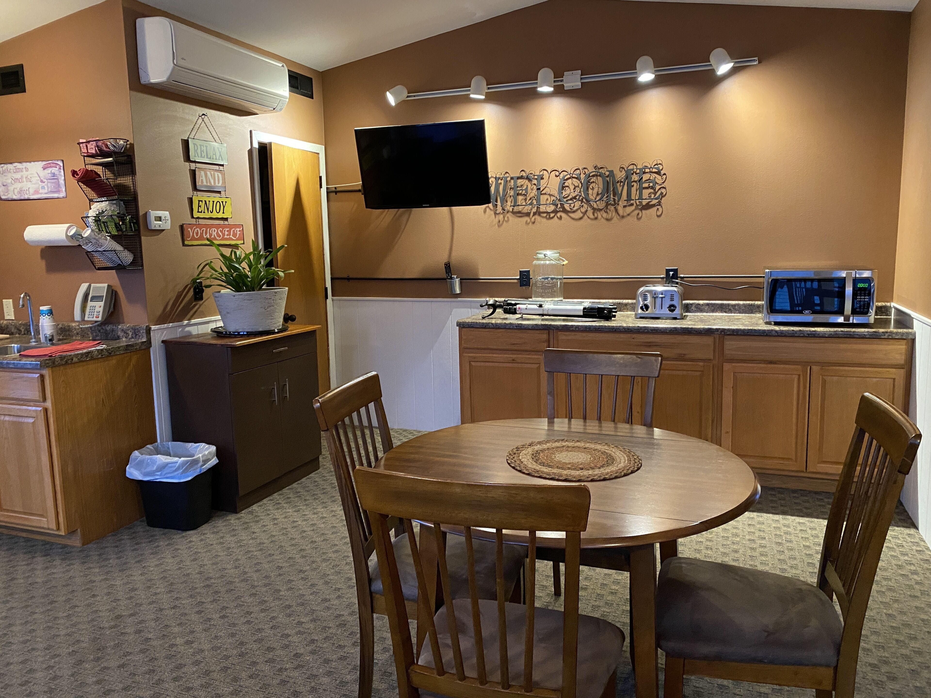 A compact kitchen with a dining area, equipped with a microwave, toaster, and a flat-screen TV.