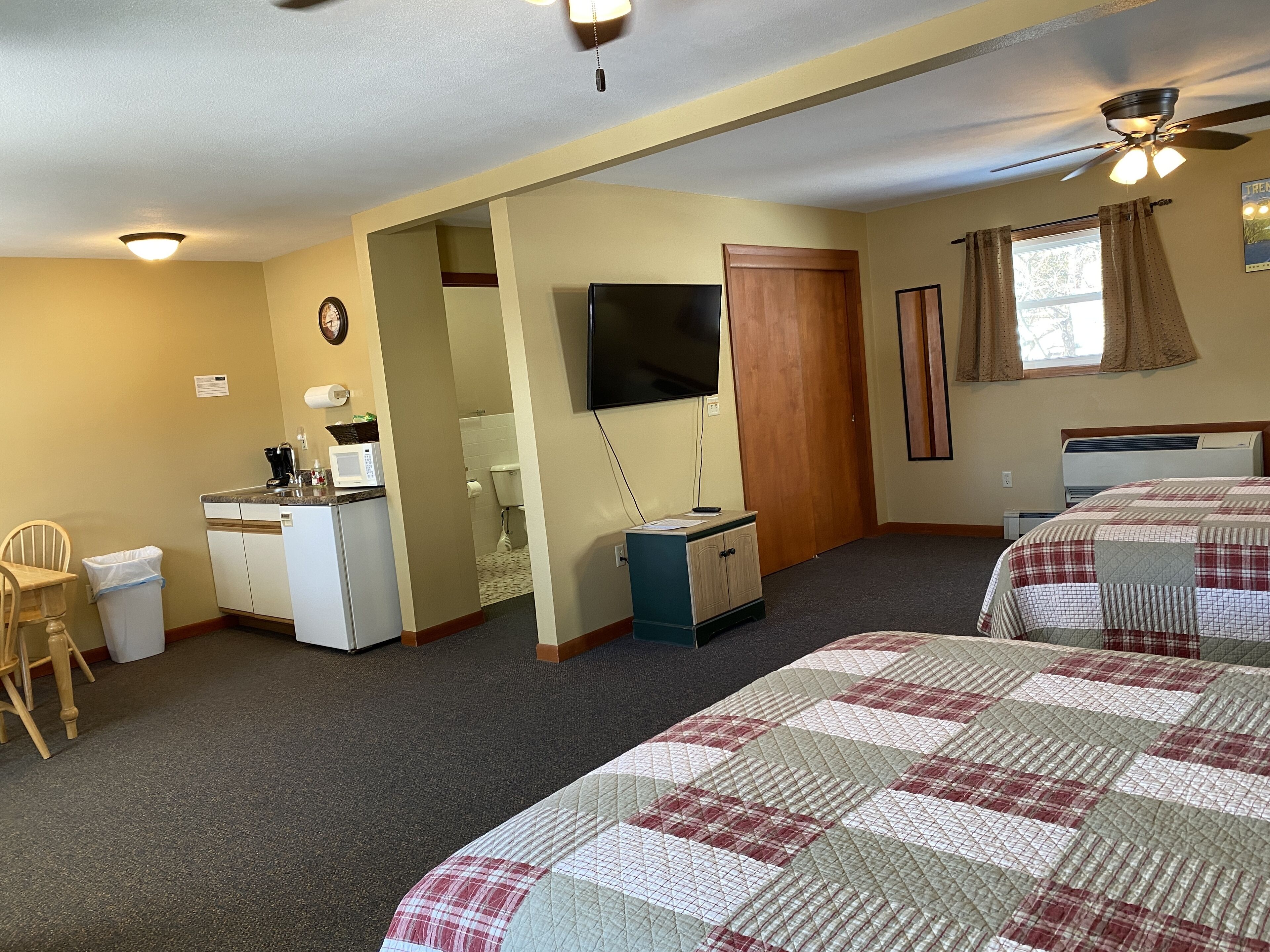 A room with two beds, a desk, a chair, a TV, and a window with curtains.