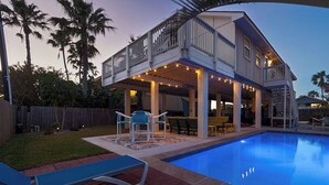 A two-story house with a pool, outdoor seating, and a covered patio area.