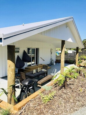 A modern house with a covered patio area featuring a table and chairs, surrounded by plants and a barbecue grill. - Cablecrest - 2 Master Suites and Grand Views (Cable Bay)