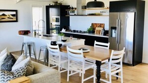 Une cuisine moderne dotée d’un îlot central, d’un coin repas avec des chaises blanches et d’un grand réfrigérateur noir.