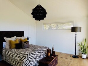A bedroom with a bed, a hanging light fixture, a floor lamp, and a window. - Cablecrest - 2 Master Suites and Grand Views (Cable Bay)