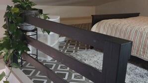 Una cama litera con suelo estampado, baranda de madera oscura y una planta en maceta.