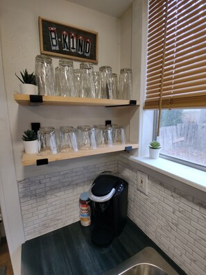 A kitchen with two wooden shelves holding glass jars and a coffee maker on the counter.