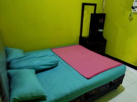 Una habitación pequeña con cama individual, cubierta y almohadas color aguamarina, una mesita de noche negra con espejo, y una pared verde.