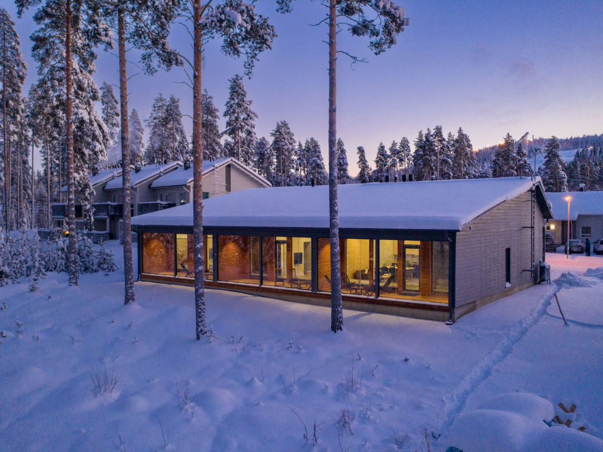 A modern building with large windows, surrounded by snow-covered trees.