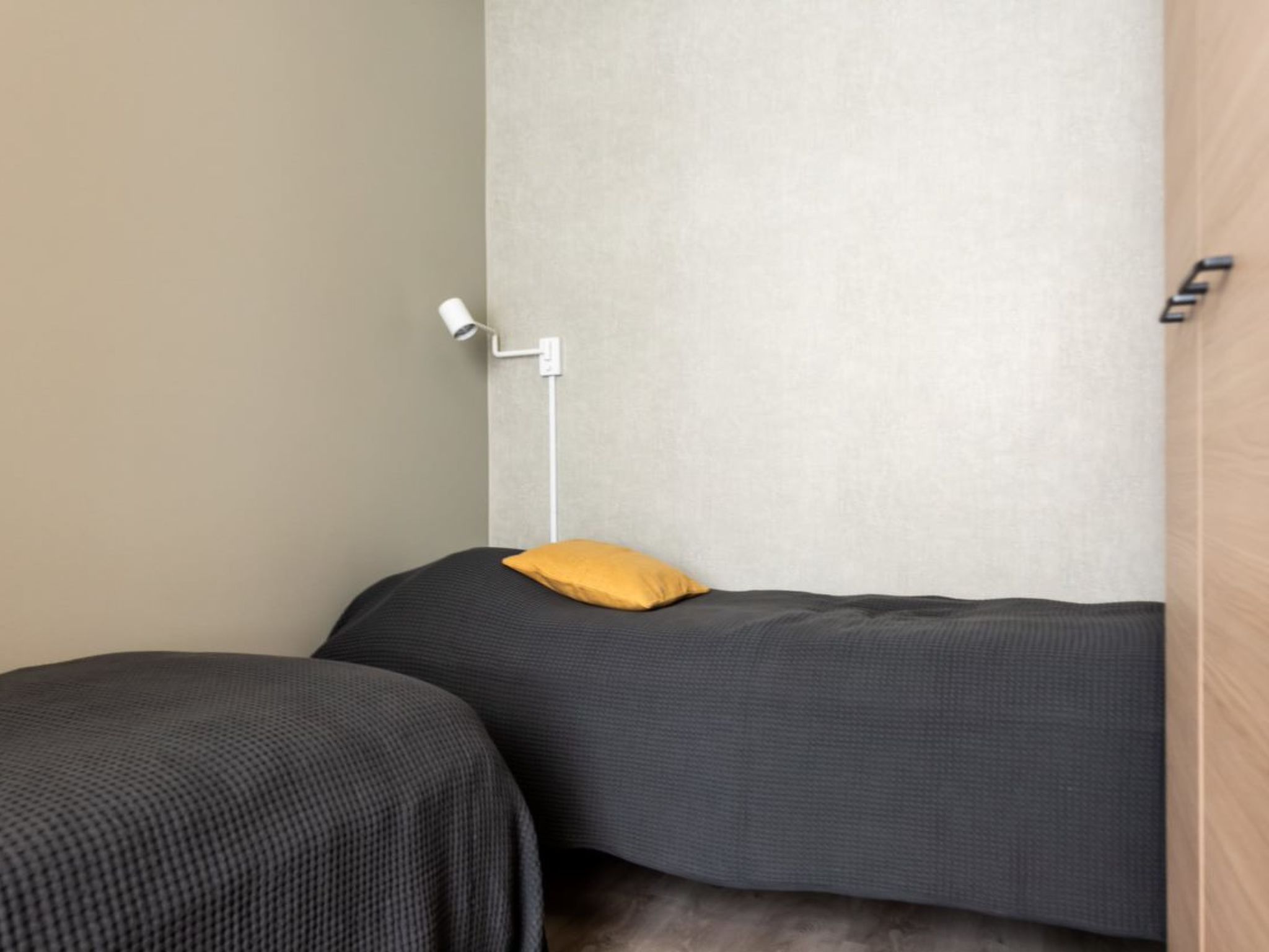 Una habitación con dos camas, una con almohada amarilla y una lámpara blanca fijada a la pared.