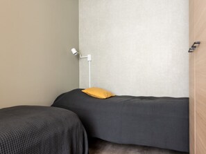 Une chambre avec deux lits, dont l’un est agrémenté d’un oreiller jaune, et une lampe blanche fixée au mur.