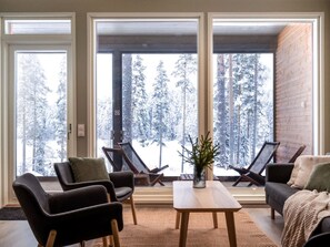 Un salon moderne avec de grandes fenêtres, une cheminée et une vue sur des arbres couverts de neige.
